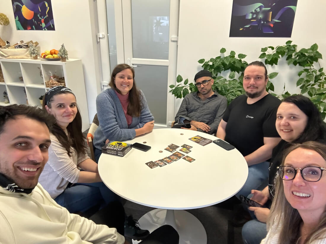 Team members sitting at a round table, playing board games and smiling for a selfie at the end of the frontend work week.
