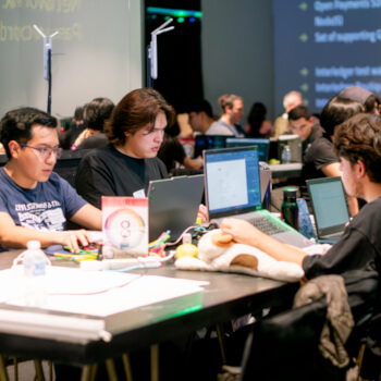 Team of developers working together on laptops at a table during the Interledger Hackathon 2025.